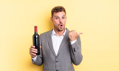 İnanamadığı için şaşırmış genç ve yakışıklı bir adam. Şarap şişesi konsepti