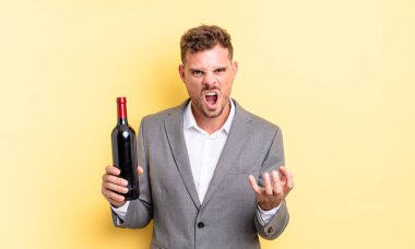 Genç ve yakışıklı bir adam sinirli, sinirli ve sinirli görünüyor. Şarap şişesi konsepti