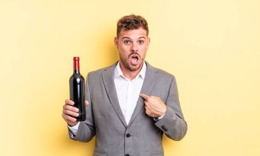 Şok olmuş ve ağzı açık, kendini işaret eden genç ve yakışıklı bir adam. Şarap şişesi konsepti