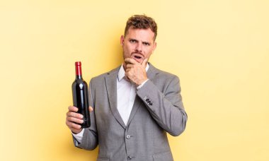 Ağzı ve gözleri açık ve eli çenesinde genç yakışıklı bir adam. Şarap şişesi konsepti