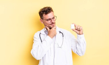 Genç ve yakışıklı bir adam mutlu ve kendinden emin bir ifadeyle gülümsüyor, elleri çenesinde. Hekim hapları şişesi konsepti