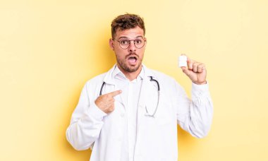 Şok olmuş ve ağzı açık, kendini işaret eden genç ve yakışıklı bir adam. Hekim hapları şişesi konsepti