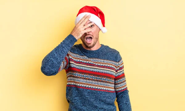 若いハンサムな男はショックを受けて怖がったり怖がったり手で顔を覆います クリスマスのコンセプト — ストック写真