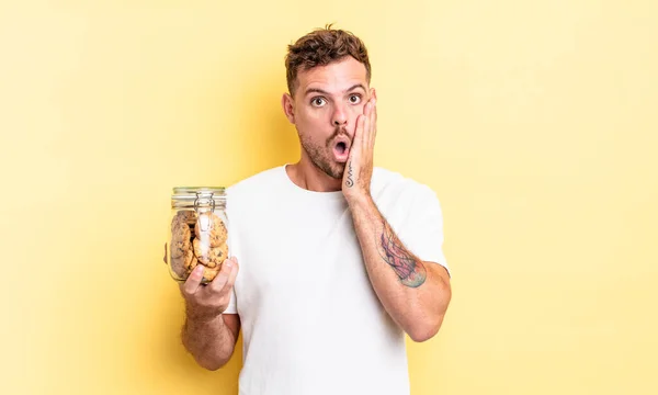 Jovem Bonito Homem Sentindo Chocado Assustado Cookies Garrafa Conceito — Fotografia de Stock