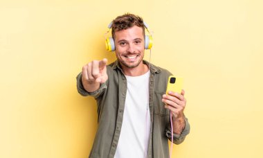 Genç yakışıklı adam kamerayı işaret ederek kulaklık ve akıllı telefon konseptini seçiyor.