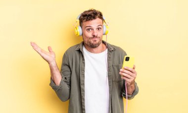 Genç yakışıklı adam şaşkın, şaşkın ve şüpheli kulaklıklar ve akıllı telefon konsepti