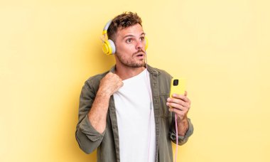 Genç yakışıklı adam stresli, endişeli, yorgun ve hayal kırıklığına uğramış kulaklıklar ve akıllı telefon konsepti