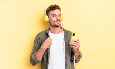 Genç yakışıklı adam kibirli, başarılı, pozitif ve gururlu kulaklıklar ve akıllı telefon konsepti
