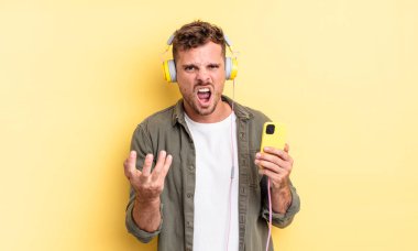 Genç ve yakışıklı adam sinirli, sinirli ve hayal kırıklığına uğramış kulaklıklar ve akıllı telefon konsepti