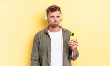 Genç yakışıklı adam üzgün ve sızlanıyor. Mutsuz bir bakışı, ağlayan kulaklıkları ve akıllı telefon konseptiyle.