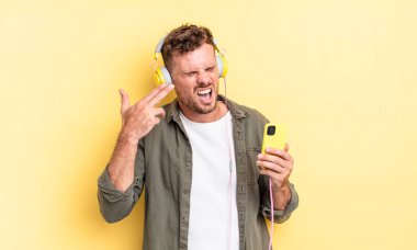 Genç yakışıklı adam mutsuz ve stresli görünüyor, intihar jesti silah işareti kulaklık ve akıllı telefon konsepti yapıyor.