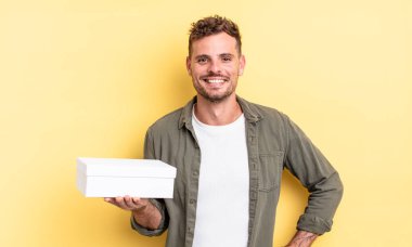 Genç yakışıklı adam mutlu bir şekilde gülümsüyor, eli kalçasında ve kendinden emin. beyaz kutu kavramı