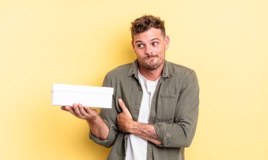 Genç yakışıklı adam omuz silkiyor, kafası karışık ve kararsız. beyaz kutu kavramı