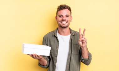 Genç yakışıklı adam gülümsüyor ve arkadaş canlısı görünüyor, iki numarayı gösteriyor. beyaz kutu kavramı