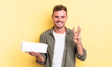 Genç yakışıklı adam gülümsüyor ve arkadaş canlısı görünüyor, üç numarayı gösteriyor. beyaz kutu kavramı