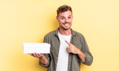 Genç yakışıklı adam neşeyle gülümsüyor, mutlu hissediyor ve bir tarafı işaret ediyor. beyaz kutu kavramı
