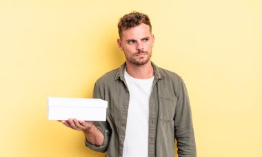 Genç ve yakışıklı bir adam üzgün, üzgün ya da kızgın hissediyor ve yan tarafa bakıyor. beyaz kutu kavramı