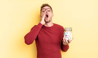 Genç yakışıklı adam mutlu hissediyor, elleri ağzının kenarında bağırıyor. jöle şekeri konsepti