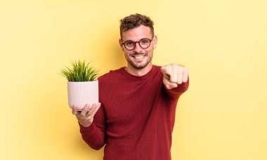 Genç ve yakışıklı bir adam kamerayı işaret ederek seni seçiyor. dekoratif bitki konsepti