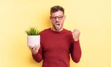 Genç yakışıklı adam sinirli bir ifadeyle agresif bir şekilde bağırıyor. dekoratif bitki konsepti