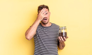 Genç yakışıklı adam şok olmuş, korkmuş ya da korkmuş görünüyor, yüzünü kahve çekirdeği konseptiyle kapatıyor.