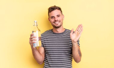 Genç yakışıklı adam mutlu bir şekilde gülümsüyor, el sallıyor, sizi selamlıyor ve selamlıyor. su kavramı