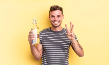 Genç yakışıklı adam gülümsüyor ve arkadaş canlısı görünüyor, üç numarayı gösteriyor. su kavramı