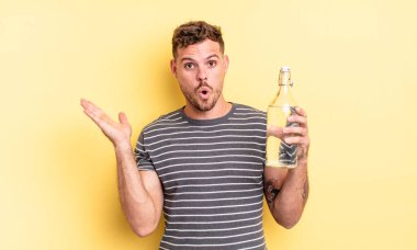 Genç, yakışıklı adam şaşırmış ve şok olmuş görünüyor. Çenesi düşmüş, elinde bir nesne var. su kavramı