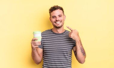 Genç ve yakışıklı bir adam, kendine güvenerek gülümseyerek kendi geniş gülümsemesine işaret ediyor.