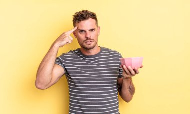 Genç yakışıklı adam kafası karışık ve şaşkın hissediyor, sana çılgın boş kase konseptini gösteriyor.