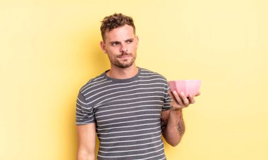 Genç yakışıklı adam üzgün, üzgün ya da kızgın hissediyor ve boş kase konseptine bakıyor.