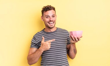 Genç yakışıklı adam heyecanlı ve şaşırmış görünüyor. Yan boş kaseye işaret ediyor.