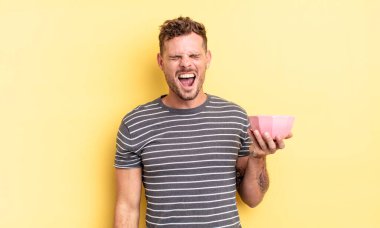 Genç yakışıklı adam agresif bir şekilde bağırıyor, kızgın boş kâse konseptine bakıyor.