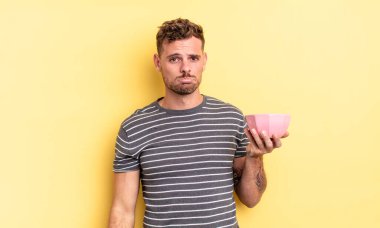 Genç yakışıklı adam üzgün ve sızlanıyor mutsuz bir bakışla ve ağlayan boş kase konseptiyle