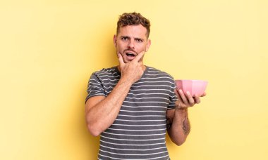 Ağzı ve gözleri sonuna kadar açık ve eli çenesinde boş bir kase konsepti olan genç yakışıklı adam.