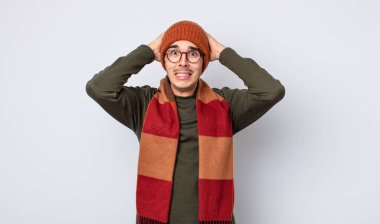 Genç ve yakışıklı bir adam stresli, endişeli ya da korkmuş hissediyor. Elleri başının üstünde. Kışlık kıyafet konsepti