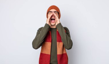 Genç yakışıklı adam mutlu hissediyor, elleri ağzının kenarında bağırıyor. Kışlık kıyafet konsepti