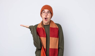 Genç, yakışıklı adam şaşırmış ve şok olmuş görünüyor. Çenesi düşmüş, elinde bir nesne var. Kışlık kıyafet konsepti