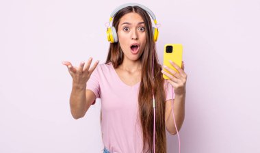 Genç ve güzel bir kadın şok olmuş ve şaşırmış hissediyor. Kulaklık ve akıllı telefon.