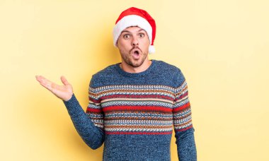 Genç, yakışıklı adam şaşırmış ve şok olmuş görünüyor. Çenesi düşmüş, elinde bir nesne var. Noel konsepti