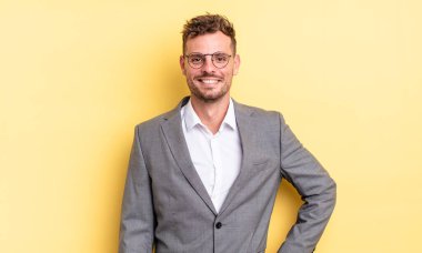 Genç yakışıklı adam mutlu bir şekilde gülümsüyor, eli kalçasında ve kendinden emin. iş kavramı