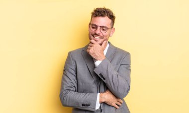 Genç ve yakışıklı bir adam mutlu ve kendinden emin bir ifadeyle gülümsüyor, elleri çenesinde. iş kavramı