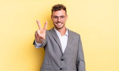 Genç yakışıklı adam gülümsüyor ve mutlu görünüyor, zafer ya da barış işareti yapıyor. iş kavramı