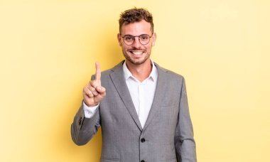 young handsome man smiling and looking friendly, showing number one. business concept