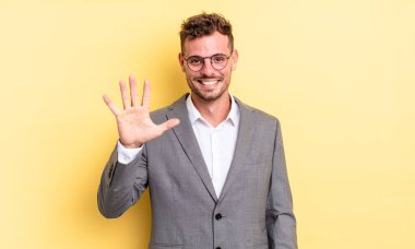 young handsome man smiling and looking friendly, showing number five. business concept