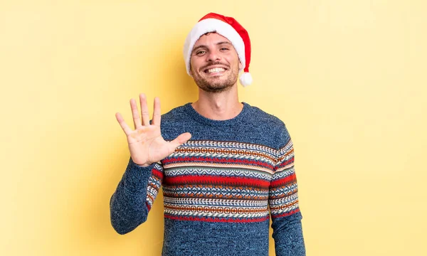 若いハンサムな男は笑顔で友好的に見える5番目を示しています クリスマスのコンセプト — ストック写真