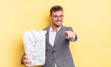 Genç yakışıklı adam kamerayı işaret ederek seni kağıt toplar çöp konseptini seçiyor.