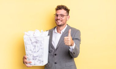 Genç yakışıklı adam gururlu, olumlu gülümsüyor. Kağıt toplar, çöp konsepti.