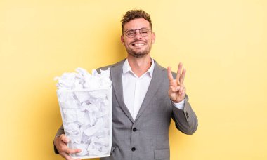 Genç yakışıklı adam gülümsüyor ve arkadaş canlısı görünüyor, üç numaralı kağıt topları çöp konseptini gösteriyor.