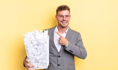 Genç yakışıklı adam heyecanlı ve şaşırmış görünüyor. Yan kağıt toplarına işaret ediyor. Çöp konsepti.